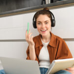 Eine Junge Frau studiert online sitzend mit einem laptop und kopfhoerern