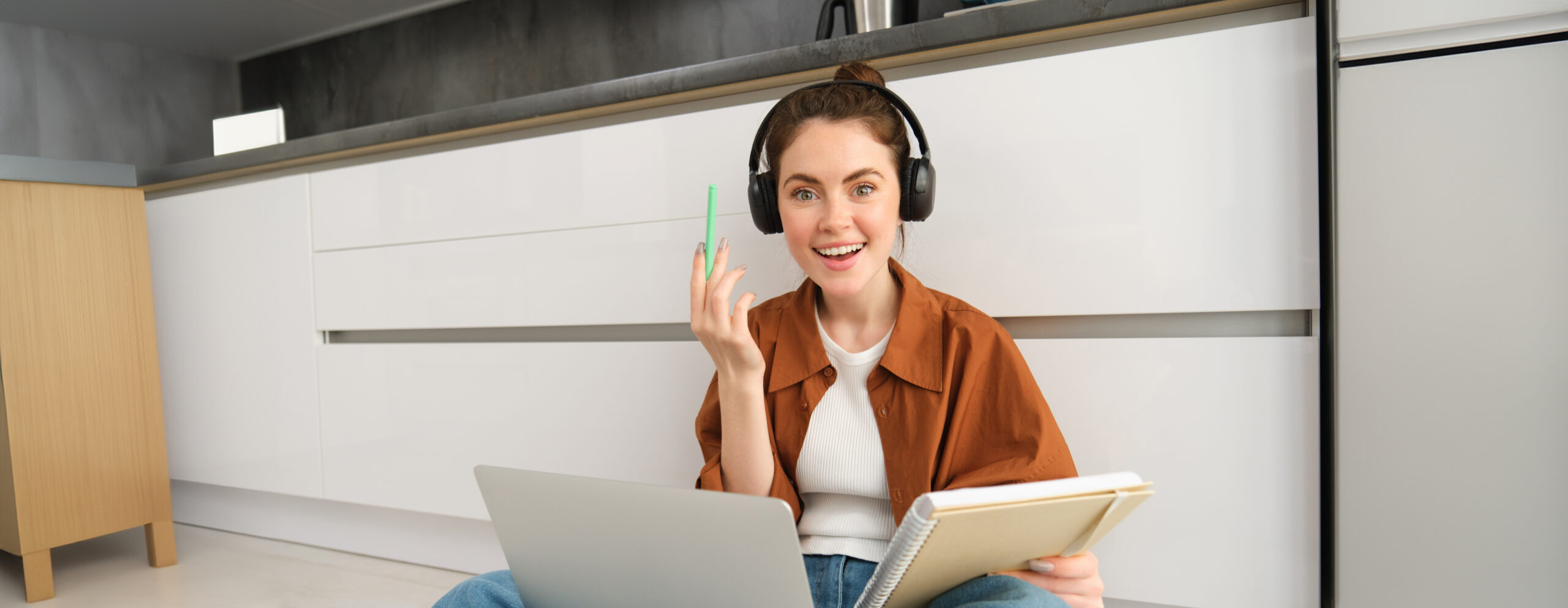 Eine Junge Frau studiert online sitzend mit einem laptop und kopfhoerern